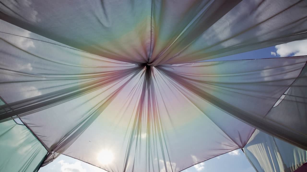 Skiftende gennemsigtig baldakin viser radiale læg under åben himmel, solen titter frem gennem en knude.