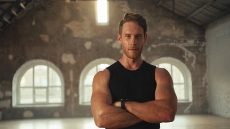 a male athlete in a black t-shirt poses against the backdrop of a sunny brick hall. portrait of a male athlete who folded his arms on his chest and pose