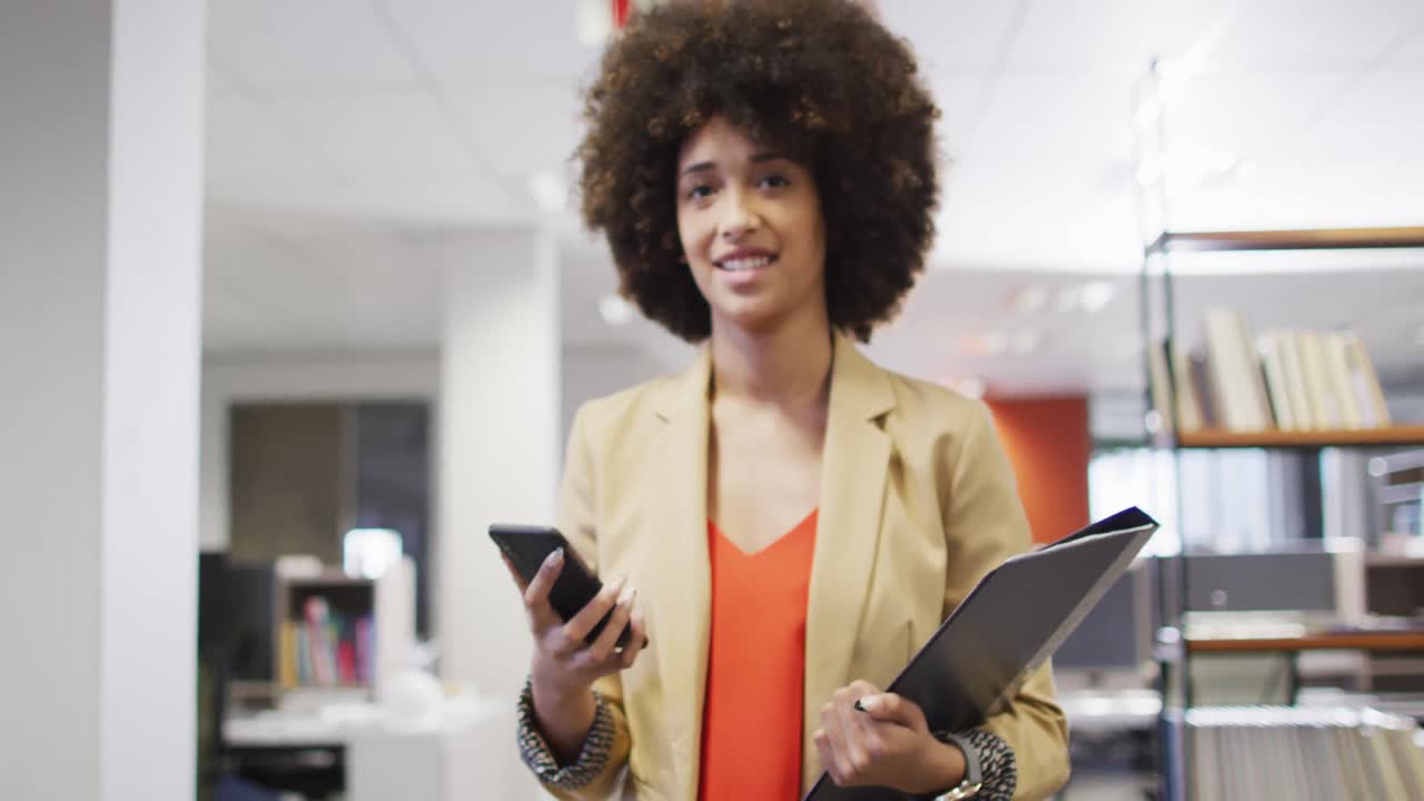 Video di una donna d'affari birazziale che cammina e usa lo smartphone in ufficio.