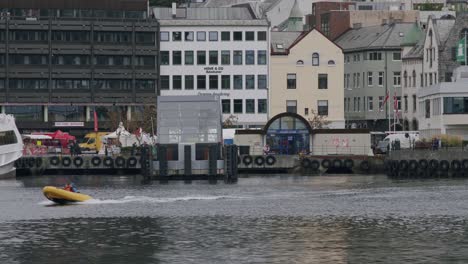 small yellow boat speeding across a harbor with buildings and waterfront in the background