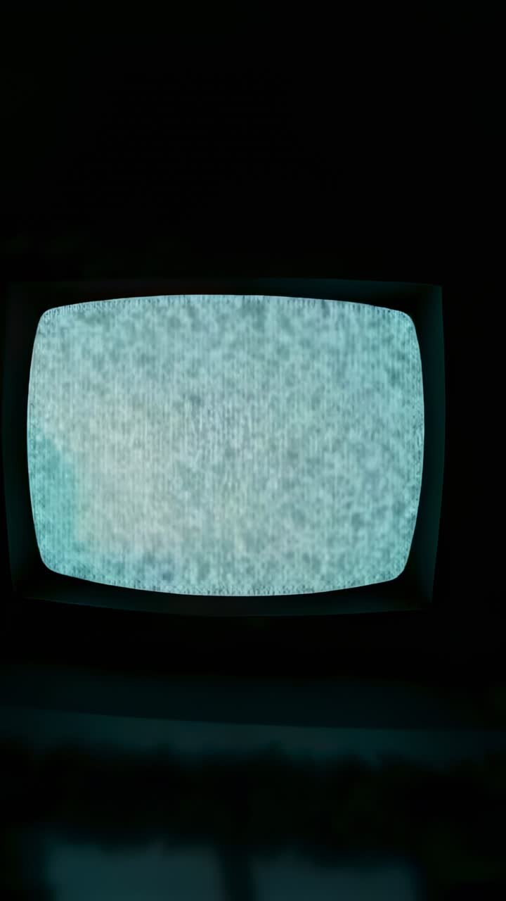 Vertical video: Losing signal, vintage CRT TV cycling through blue-gray static in dark room