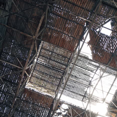 ruined plant interior with pitted roof and the sun shines inside. empty space of abandoned building with many damaged hole in the walls and the ceiling. camera moves up.