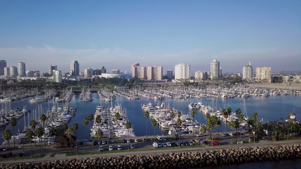 Aerial rotate right of Shoreline Yachts docked on blue water near long beach and downtown skyline in background in los angeles