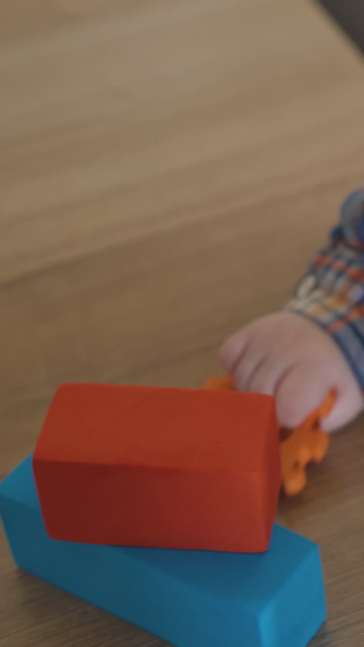 funny blond haired baby nibbles soft rubber toys leaning on low wooden table with color cubes at white wall closeup