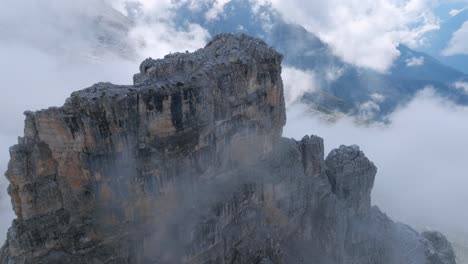 aerial oribiting shot of rocky peak in dolomites mountains with white clouds covering valley