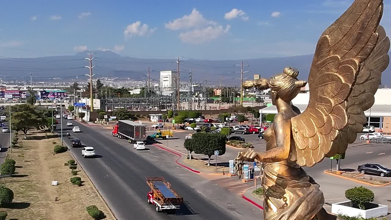 Bronze angel statue overlooking busy street in Jiutepec, Morelos. Drone aerial, static view