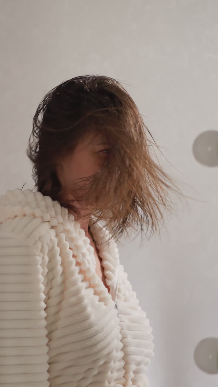 mujer morena escucha canciones enderezando el cabello mojado después de lavarse. mujer alegre se mueve a la música en el reflejo del espejo en el baño en cámara lenta