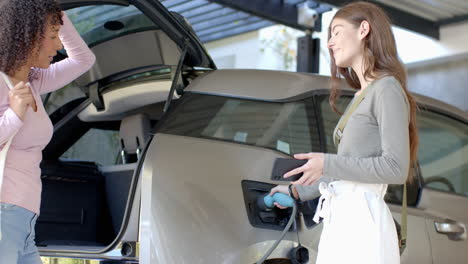 charging electric car, woman holding smartphone and smiling at female partner