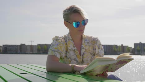 cute young woman reads a book, sitting on the pier next to the water