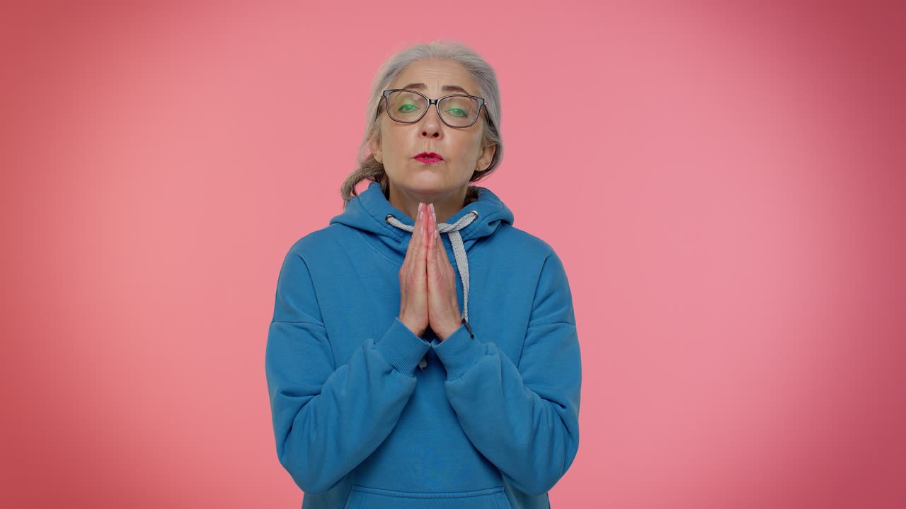 Mature old woman praying to God making wish asking with hopeful imploring expression begging apology