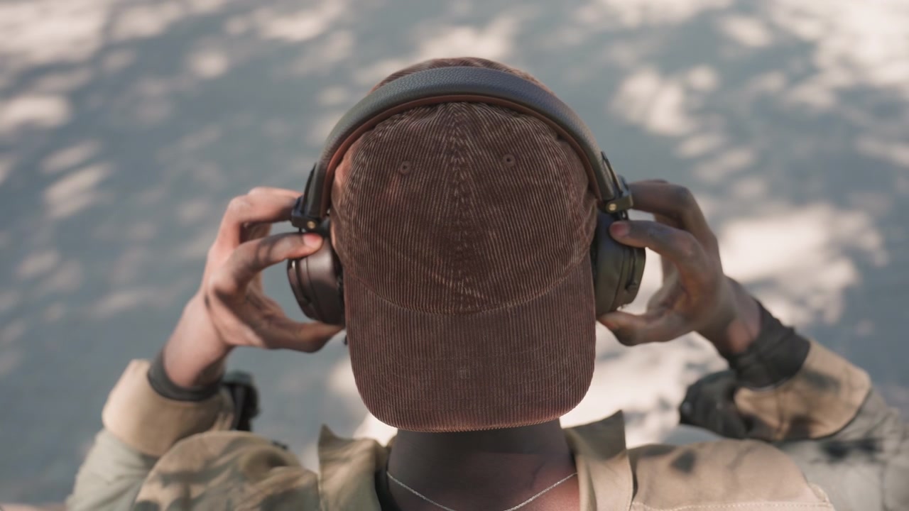 Close-up seseorang memakai headphone dan menyesuaikannya dengan kedua tangan, berfokus pada interaksi antara jari-jari mereka dan perangkat audio. Orang tersebut mengenakan pakaian kasual luar ruangan