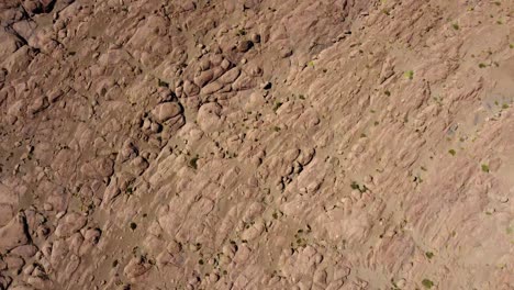 aerial looks down onto barren rock landscape to desert sand in bolivia