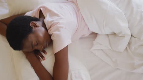 african american woman sleeping and wearing white pyjamas in her bedroom