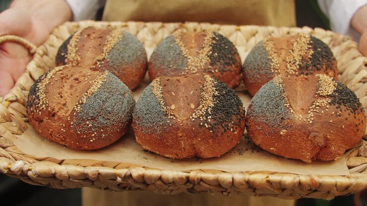 The baker holds in hands a of fresh bread with black poppy garnish on top close-up. Artisan bread is making by skill bakers using natural and high-quality ingredients. Food with health and flavour benefits.
