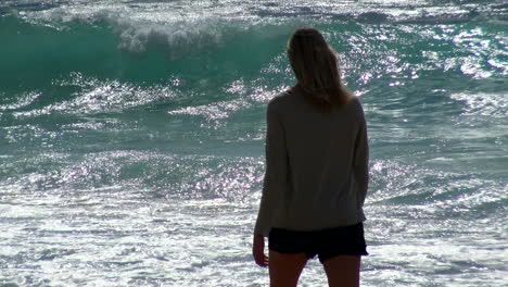 Young-woman-walks-pensively-along-beach-and-surf-with-long-lens---shimmering-sun-at-Poipu-Kauai's-Shipwreck-beach-in-Hawaii,-waves-in-background,-4k