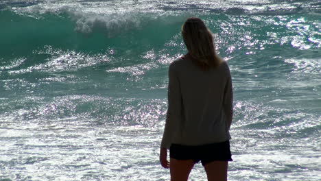 young woman walks pensively along beach and surf with long lens - shimmering sun at poipu kauai's shipwreck beach in hawaii, waves in background, 4k