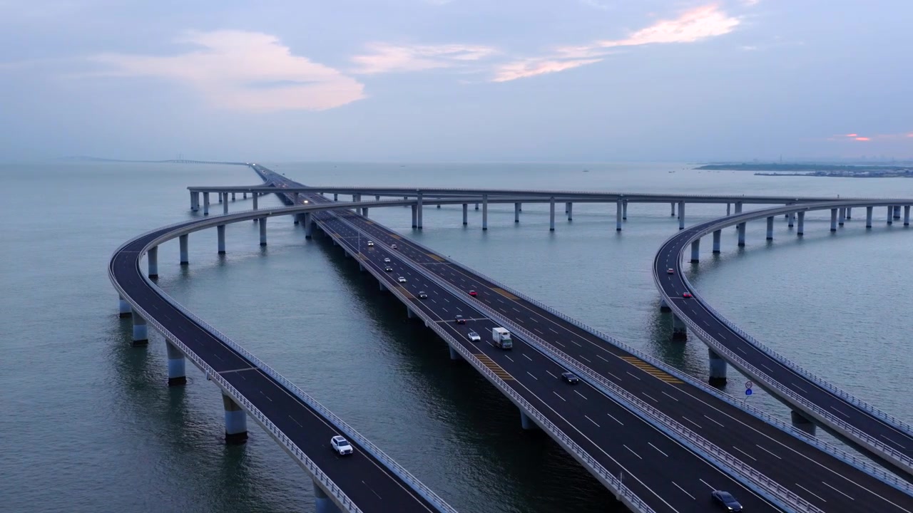 Dronebillede fra luften af Qingdao Bugtens Havbro under den blå time ved skumring, tunge lastbiler og køretøjer kører på havviadukten, storslået kinesisk transportinfrastruktur.