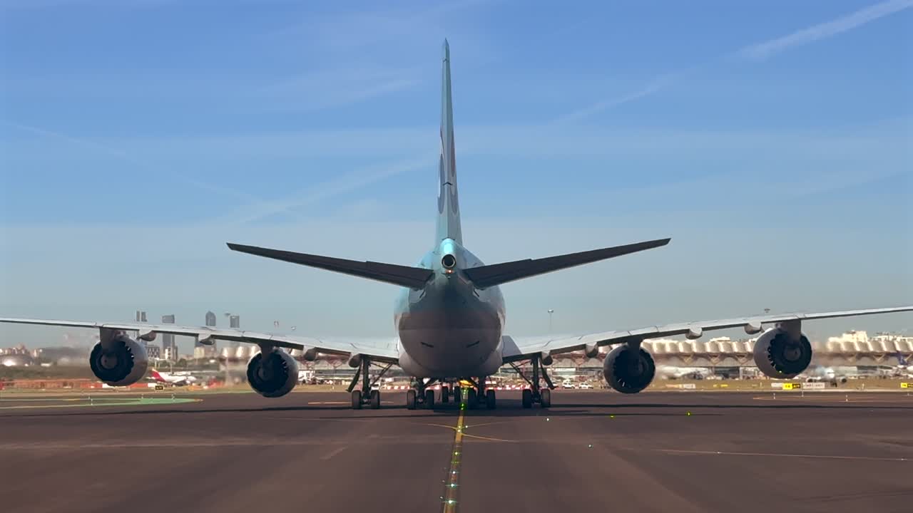 Closeup view of the rear fuselage of a massive 747 wide-body jet taxiing through Madrid airport, illuminated by the sunset light, with ther Terminal 4 and Madrid skyline at the background