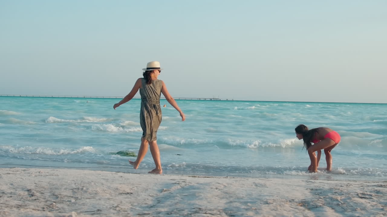 해변에서 즐겁게 지내는 유쾌한 가족, 해변에서 산책하는 어머니와 딸.