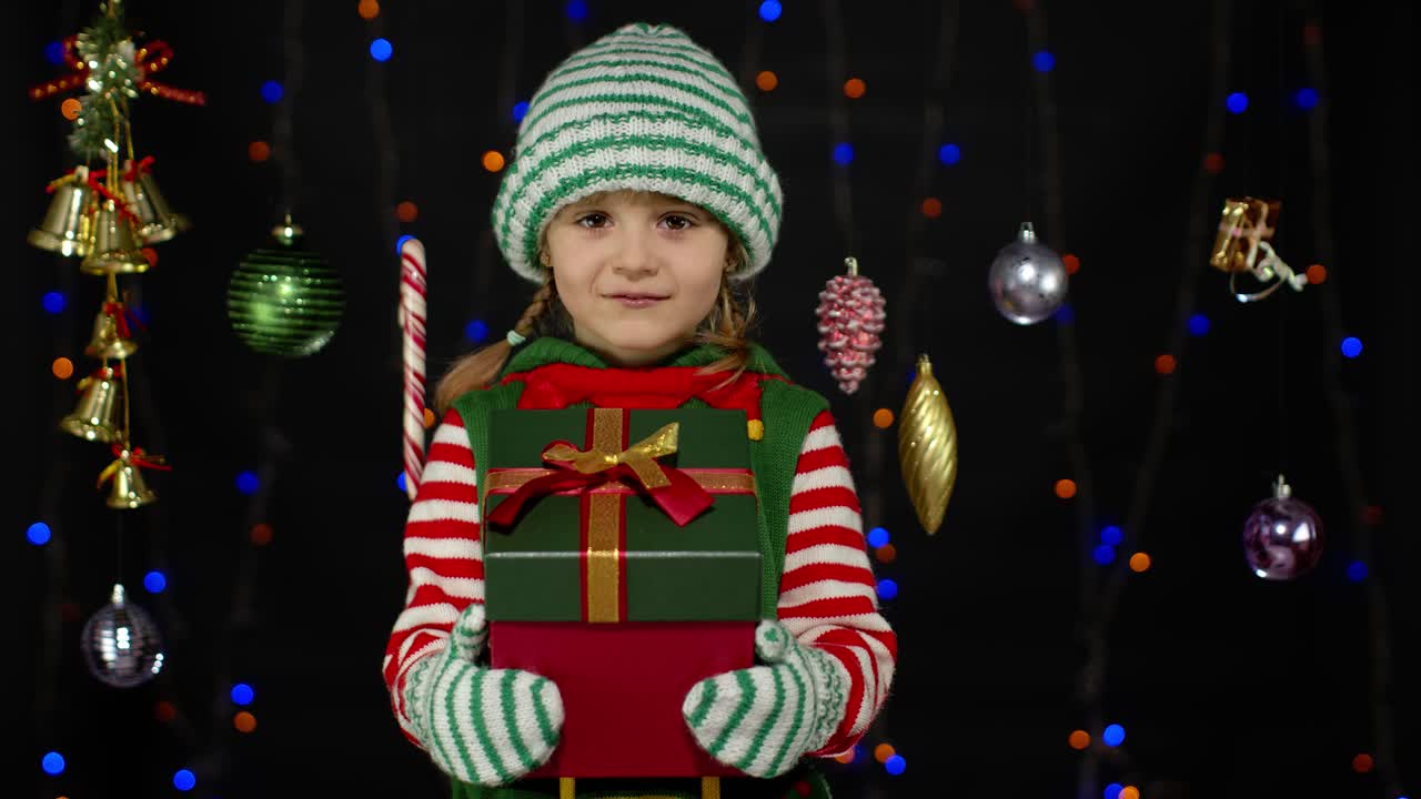 Dívka jako vánoční skřítek, pomocník Santa Clause, dává dárkovou krabici do kamery. Šťastné novoroční svátky.
