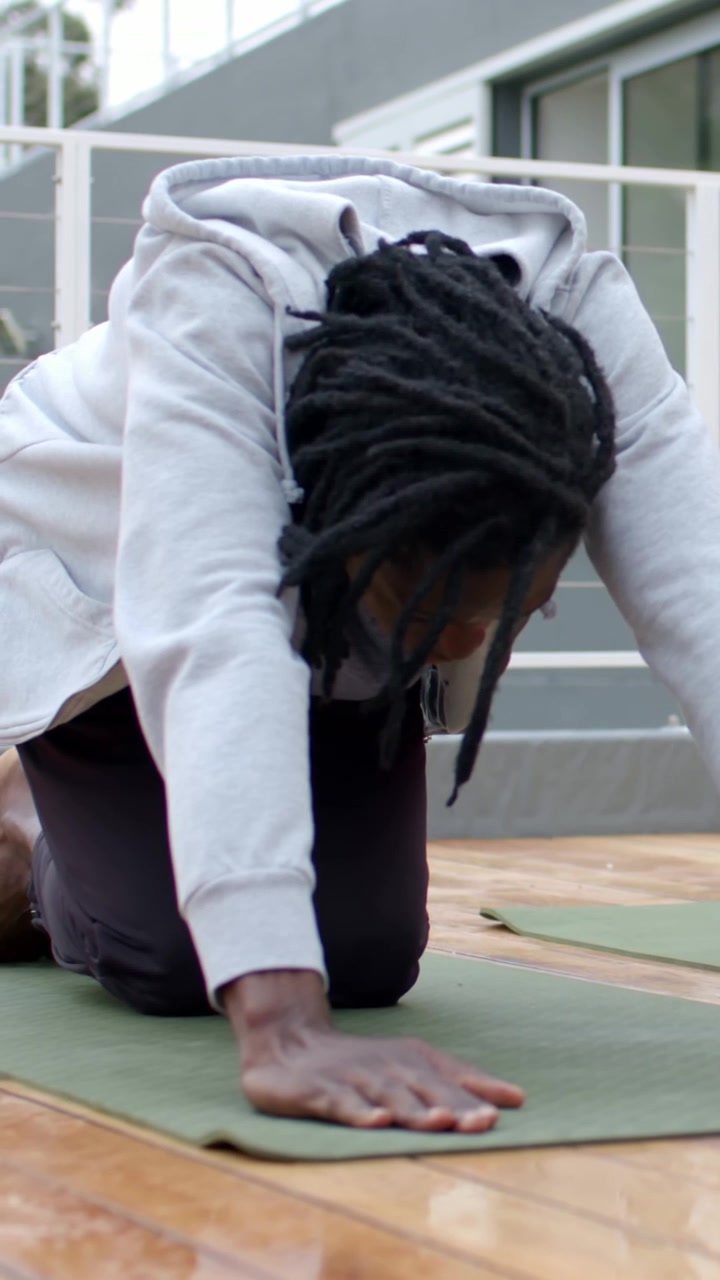 Vertical video: Leaning man starting kneeling, stretching on deck green mat hoodie for back stretch