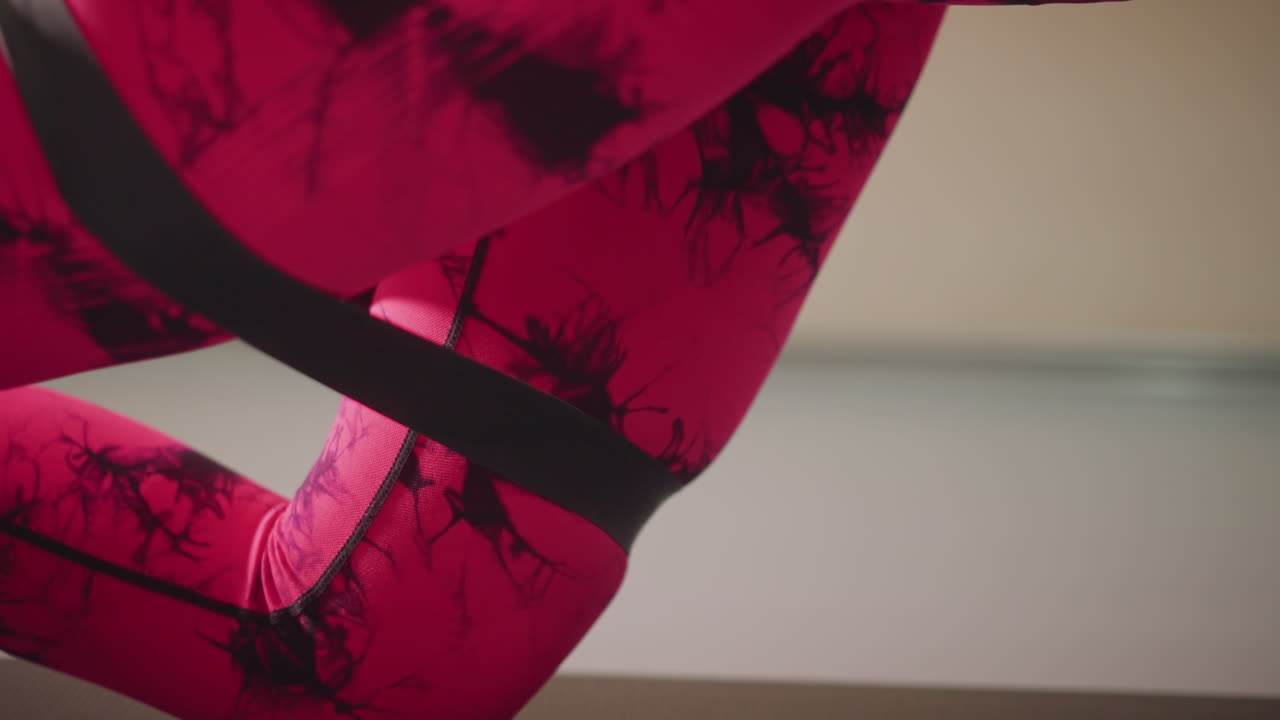 Primo piano del piede di una ballerina su tappetino da yoga, con leggings tie-dye rosa e una fascia di resistenza nera, che esegue una flessione plantare controllata in una luce soffusa da studio, focalizzata su tecnica, riscaldamento, precisione e forza della caviglia.