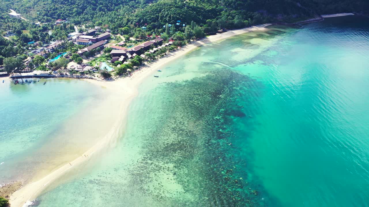 Beautiful coral reef patterns under calm turquoise lagoon surrounding white sandy stripe on beach of tropical island with vacations resort in Thailand