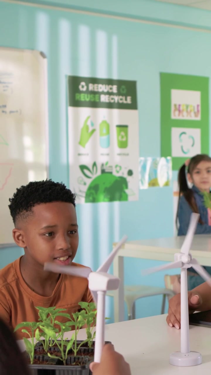 Vertical video: Teacher spinning model guiding orange tee boy spinning turbine in class for science