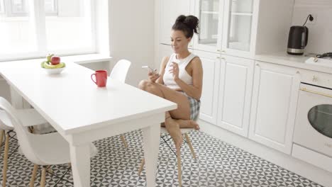 Woman-with-teléfono-sitting-at-kitchen