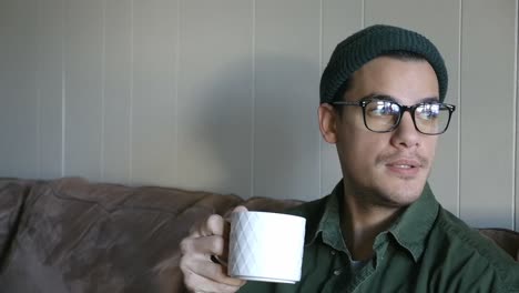 joven con gorra y gafas bebe café de una taza cu estática