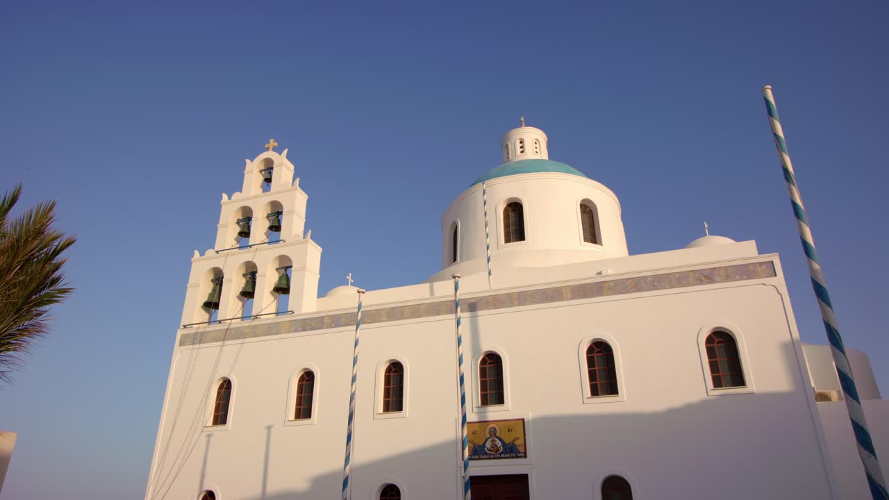 A stunning whitewashed Greek island church with a blue dome basks under the bright summer sun, framed by clear skies and the Aegean Sea—capturing the timeless beauty of Greece