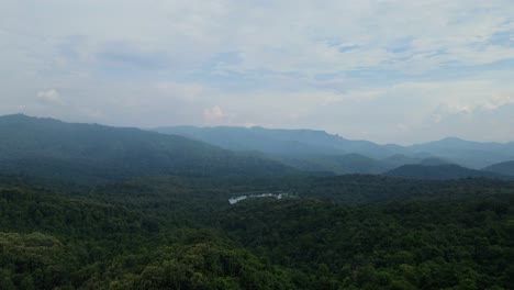an aerial footage towards a lush rainforest, mountains in the horizon, and lake in the middle glittering like a gem, thailand