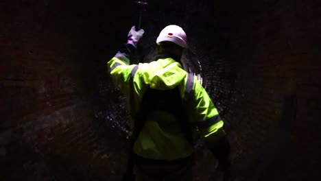 un trabajador del distrito de alcantarillado conduce el camino con una luz por un antiguo túnel de alcantarillado del siglo xix