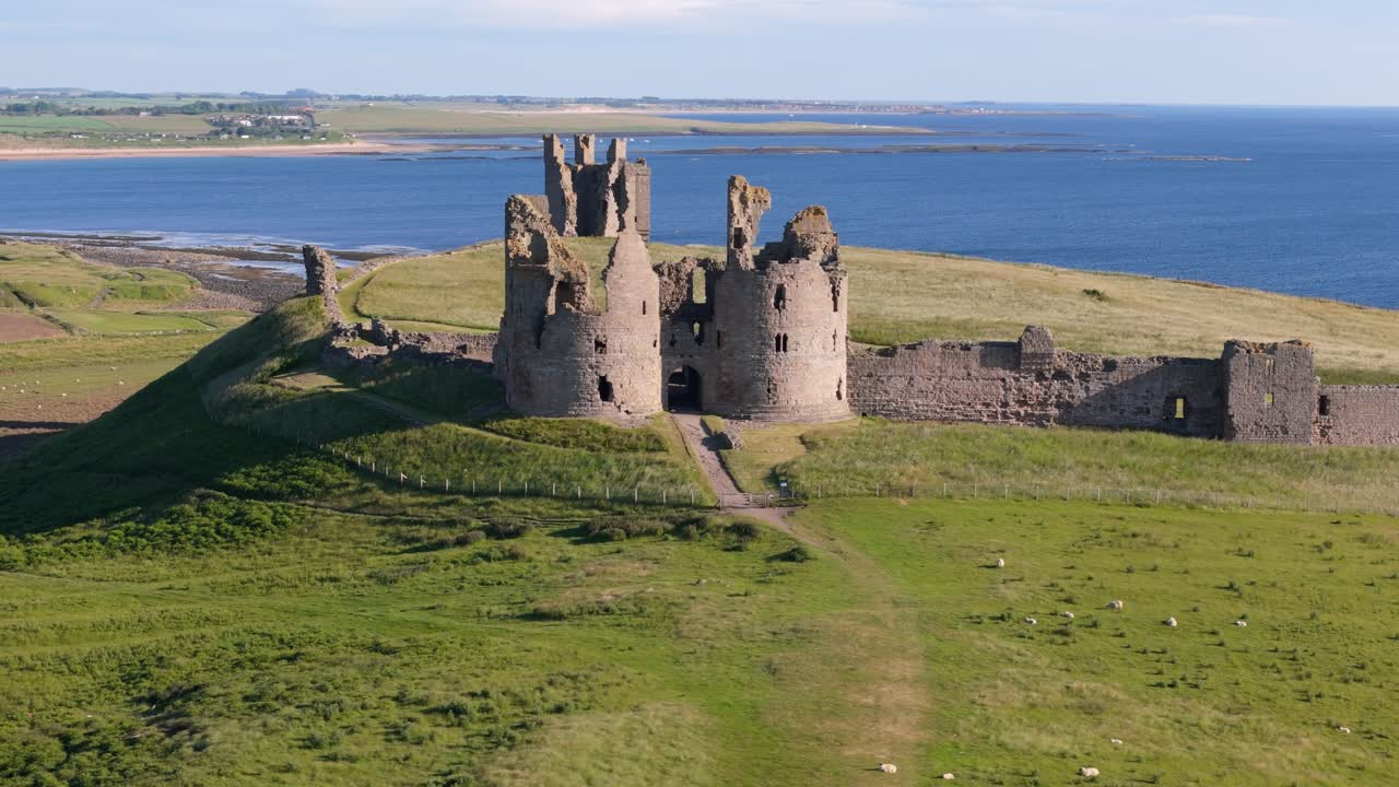 Aerial footage of Dunstanburugh castle ruins on a summer morning with no people