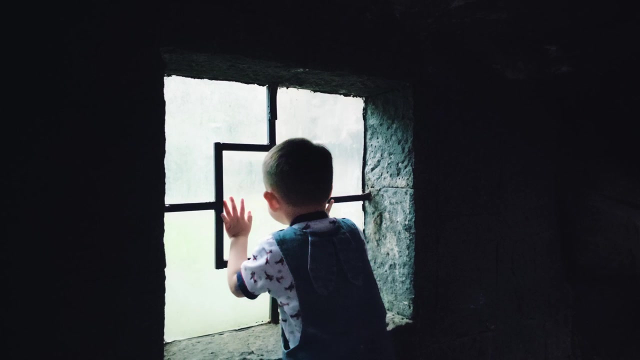A small child, inside a dimly lit mammal habitat enclosure at Chapultepec Zoo, peers through an observation window. He appears to be searching for something, possibly responding to a call, but finds n