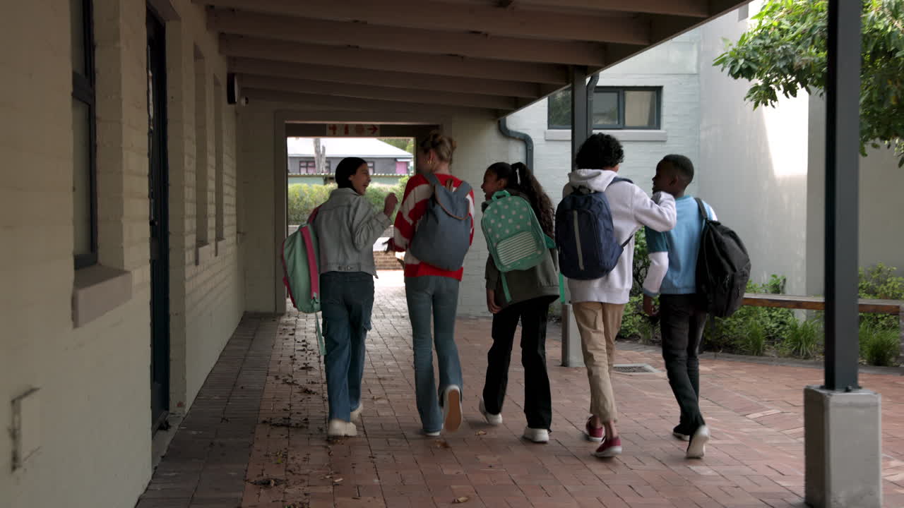 Multiracial students walking together with backpacks in school hallway, enjoying conversation