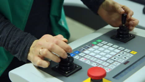 Worker-managing-production-process-with-two-joysticks-on-control-panel