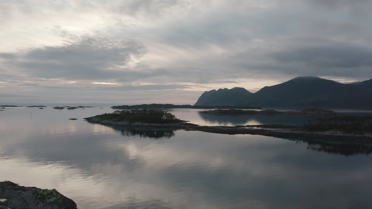 Drone view over Senja’s tranquil coast, rocky islets, and distant mountain silhouettes