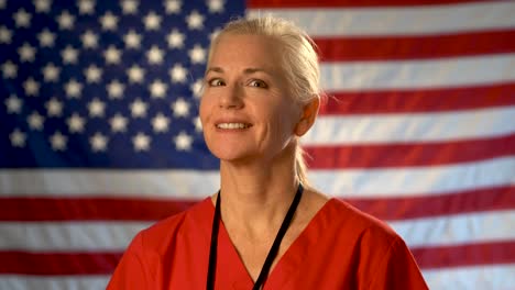 medium tight portrait of nurse looking to the left and then at camera, relieved, happy and nodding her head with american flag behind her