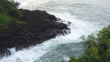 HD-120fps-Hawaii-Kauai-static-overhead-view-of-waves-crashing-on-rocky-shoreline-with-greenery-in-foreground