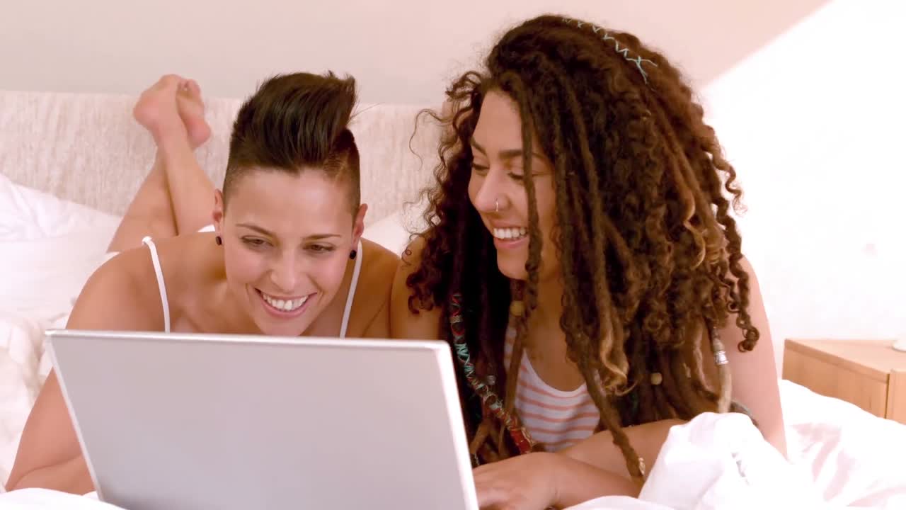 una pareja feliz de lesbianas usando una computadora portátil en la cama.