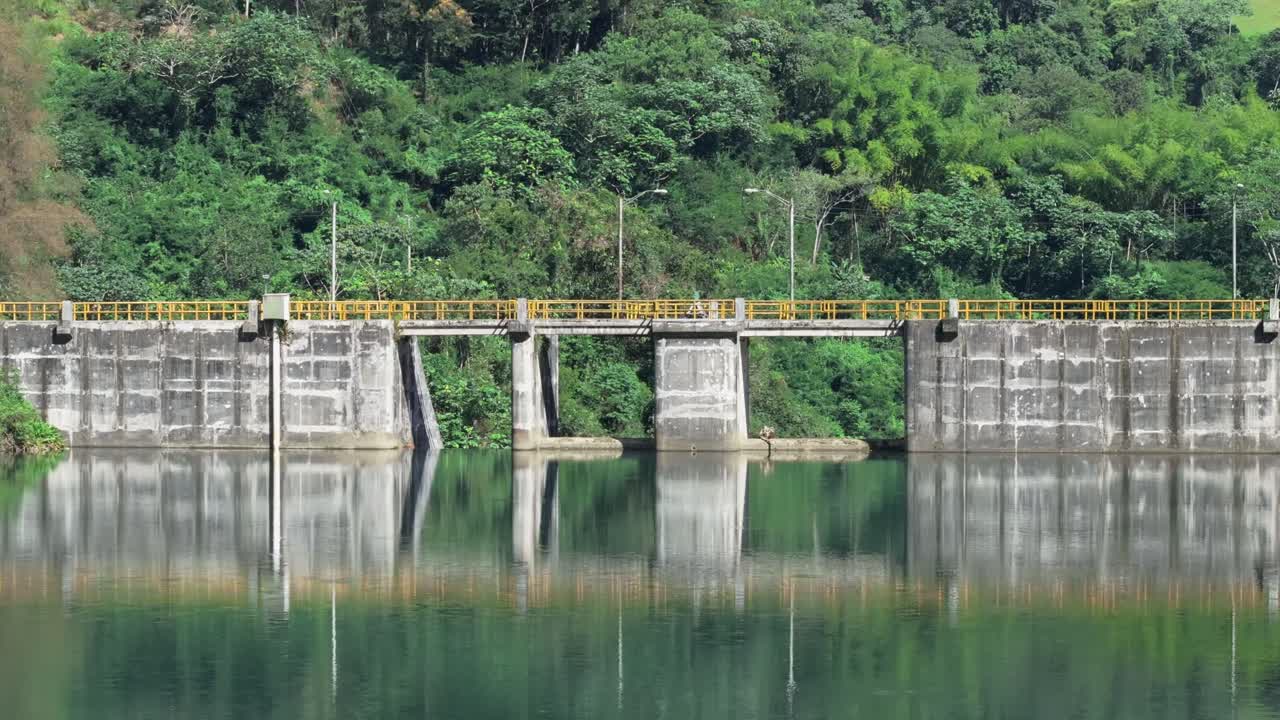 Massive dam of a water reservoir, artificial lake, exotic forest, aerial forward