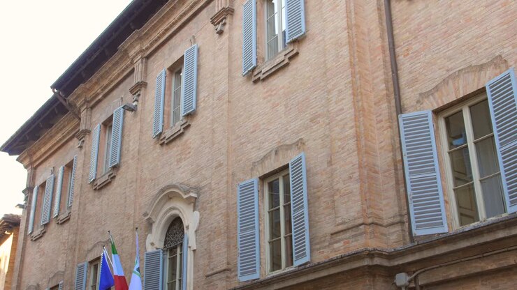 Inquadratura dal basso di un edificio storico con le bandiere dell'UE e italiana appese sul davanti a Urbino, Italia. Architettura del centro storico.