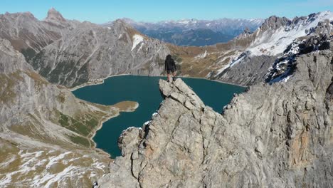 A-young-man-is-taking-careful-steps,-walking-up-to-the-top-of-a-cliff-to-see-the-amazing-view-of-Lunersee-in-Switzerland-with-its-heart-shaped-lake-below