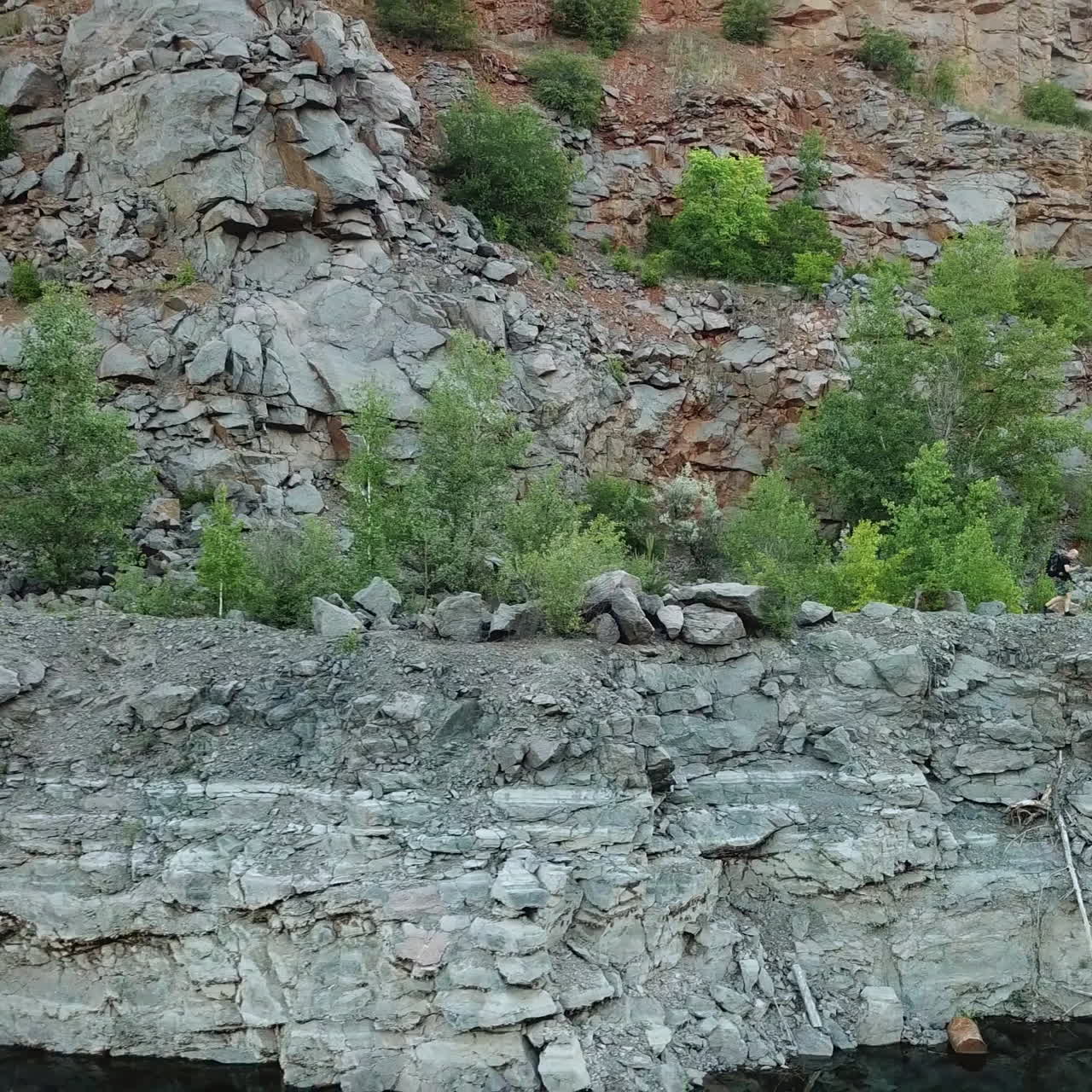 A tourist with a backpack walks around the lake on the background of a quarry on a warm day. Gray background. Camera motion to right.