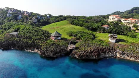 Fliegende-Drohne-Am-Strand-Von-Roatan-Mit-Klarem,-Blauem-Krustenwasser-Und-Häusern-In-4k