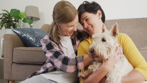 Caucasian-woman-kissing-her-wife-on-forehead-while-she-plays-with-her-dog-at-home