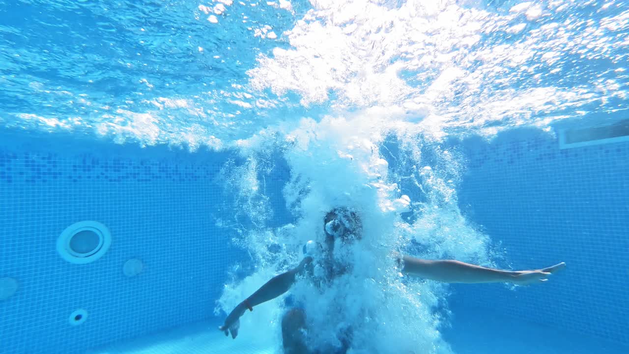 An energetic dive into a swimming pool. Handsome young man swimming in pool, underwater view