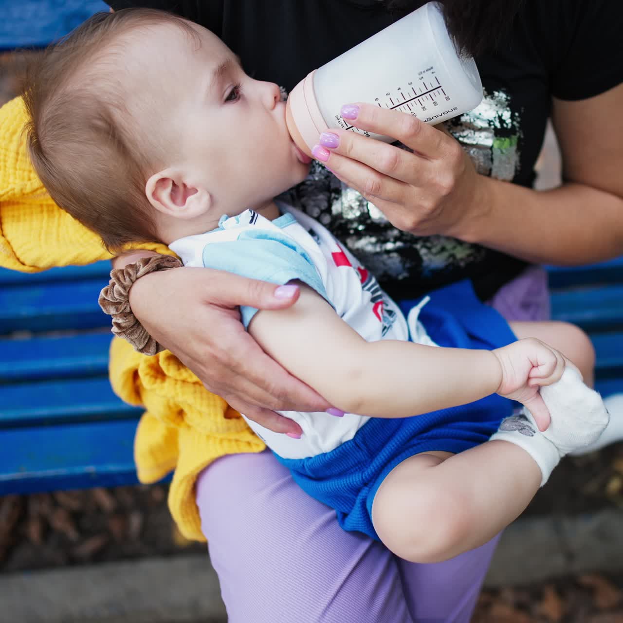 Bambino adorabile e carino che beve dal biberon e si tocca i calzini. La mamma che allatta il bambino all'aperto. Primo piano