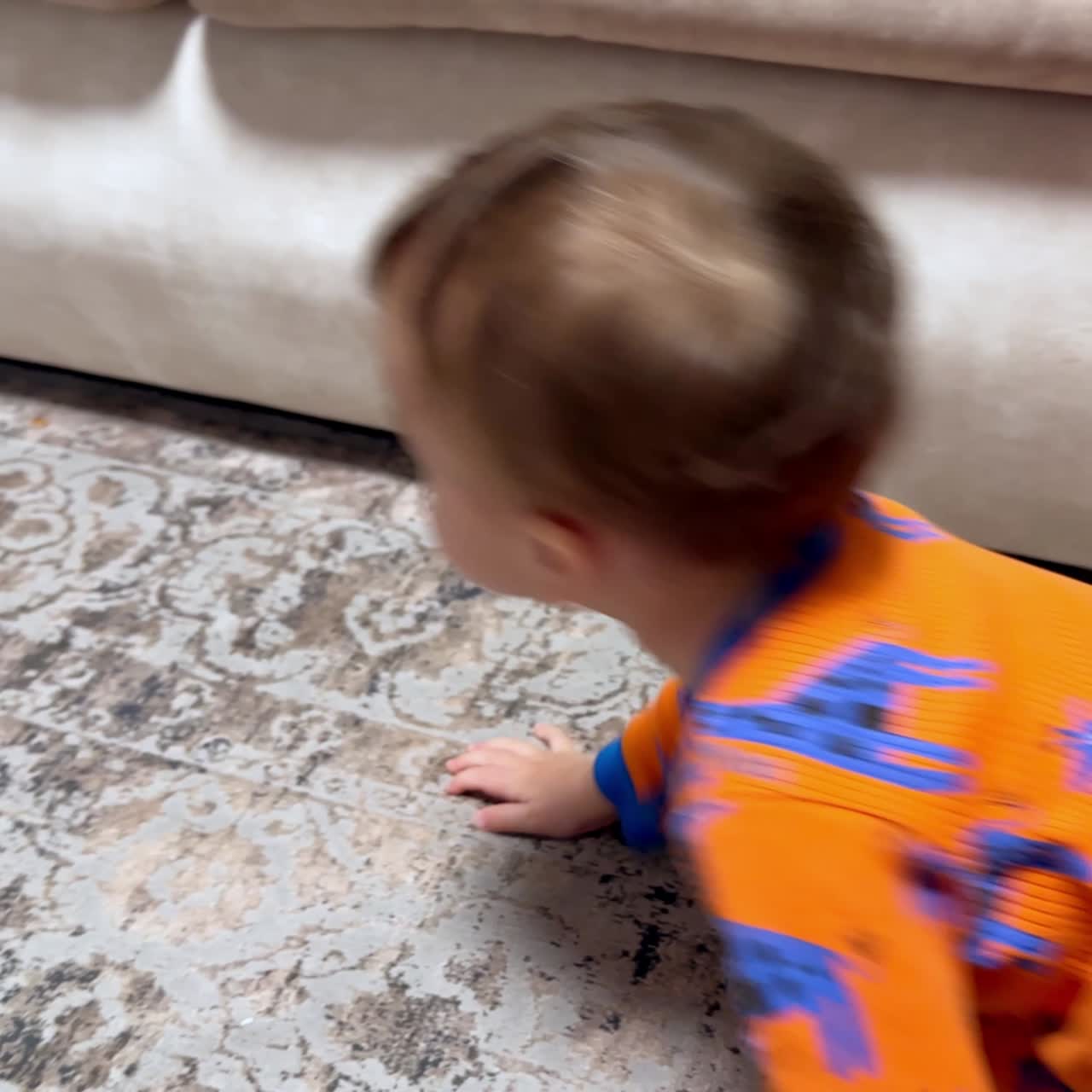 Little baby in orange romper with giraffes crawls by the floor. Happy kid finds the pacifier and gives it to somebody